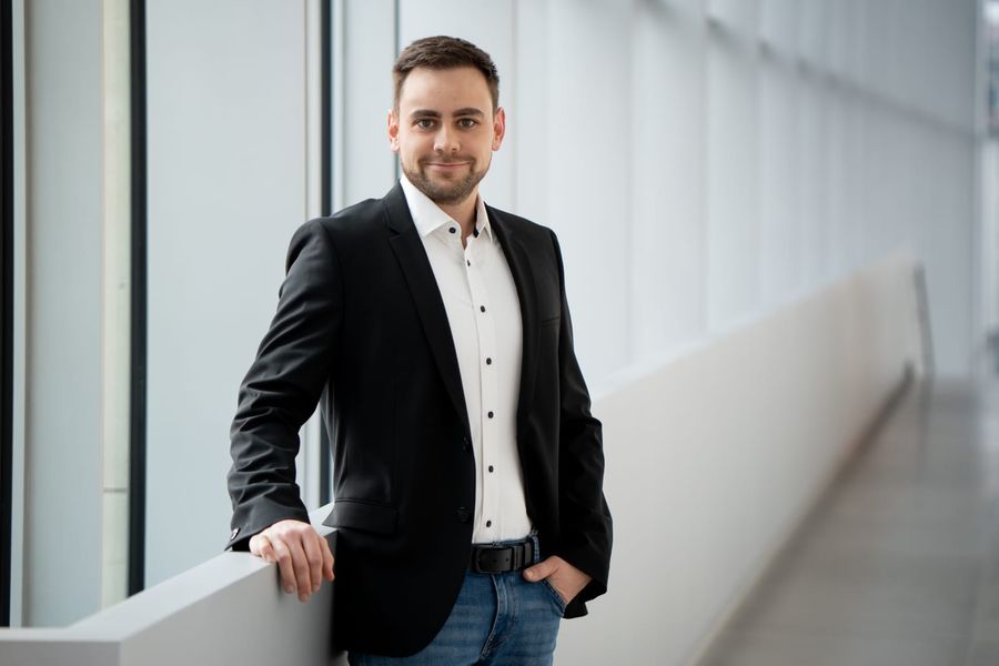 Markus Mösch im Anzug, lehnt an einer Brüstung in einem modernen Gebäude